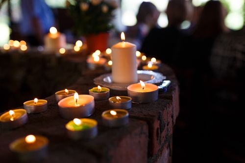 Image is of a bunch of lit white pillar candles at a memorial service, concept of Fullerton wrongful death lawyer