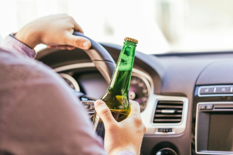 A man is holding a bottle of alcohol while driving a car