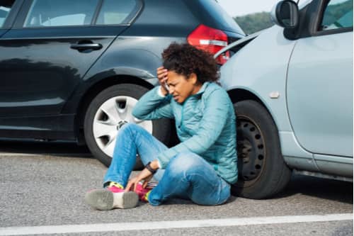 A woman is sitting on the sidewalk near the car after the accident