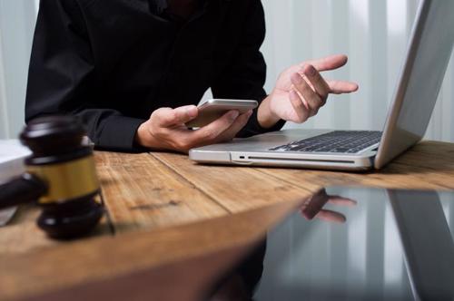 A person is sitting at a laptop and holding a phone in their hand