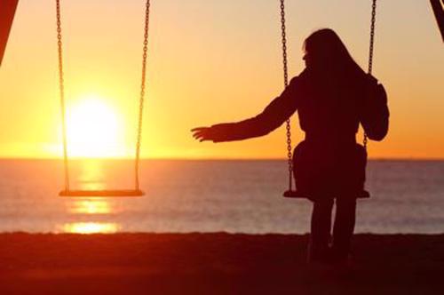 a woman is swinging on a swing facing the ocean