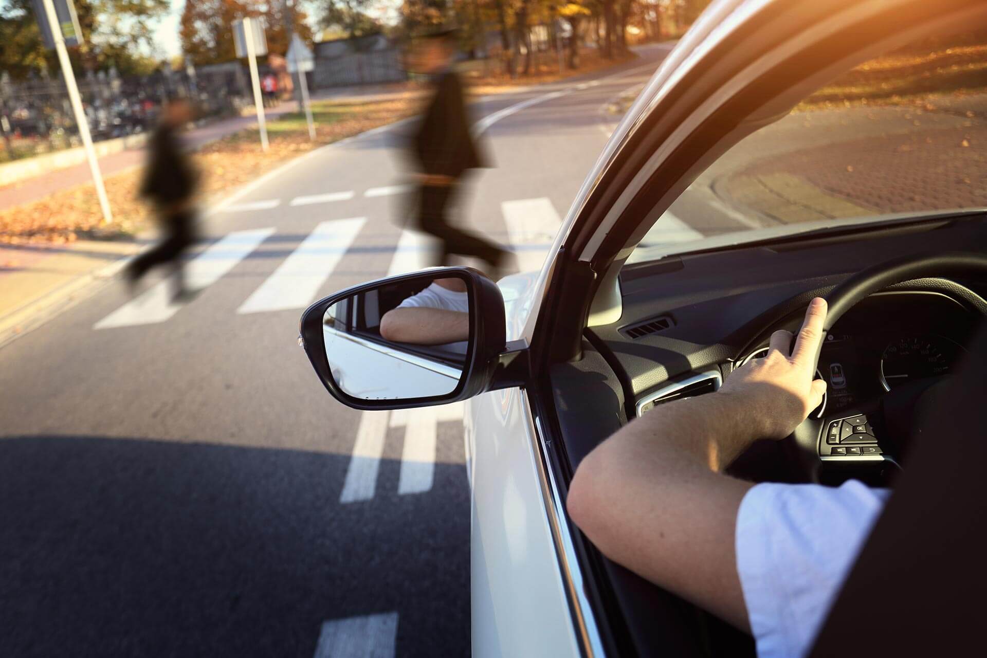 a driver is at the wheel of a car while people are crossing the road at a crosswalk