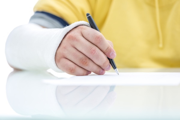 Closeup of fractured male hand in plaster signing insurance claim.