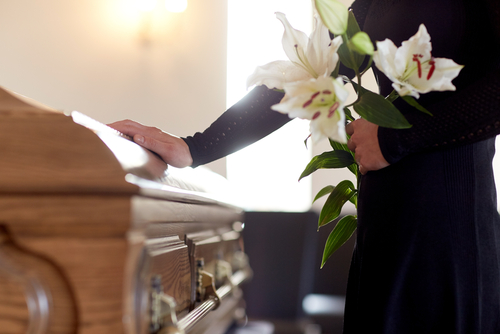 This is an image of a woman holding flowers with hand on coffin of loved one