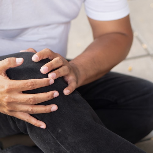 This is an image of a man who is holding his injured knee while sitting on the ground.